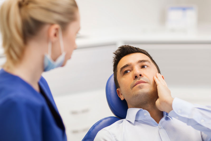 Image of a new patient holding the side of his jaw while talking to a dental assistant about a root canal.