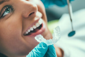 Close up photo of a doctor holding a clear aligner up to a female patient’s teeth.