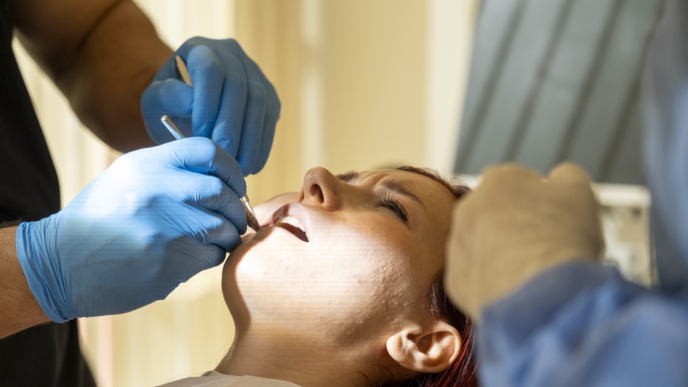 Image of a dentist in a bright office explaining options to a smiling patient, including a pamphlet titled "Veneer Options & Lifespan".