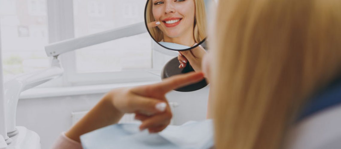 Young smiling satisfied fun happy calm woman 20s reflected in mirror sitting at dental office