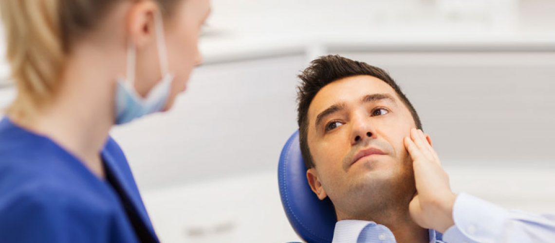 Image of a new patient holding the side of his jaw while talking to a dental assistant about a root canal.