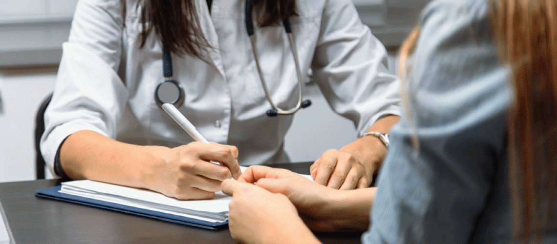 Close up of a female doctor filling up an application form while consulting patient